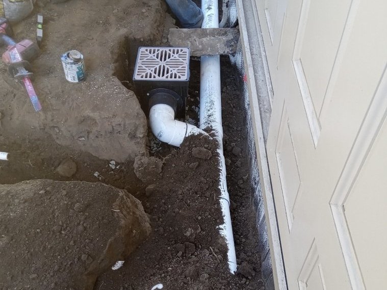 Catch basin with PVC line running along the side of a home