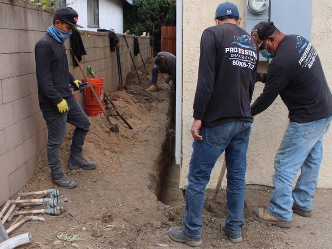 Crew members reviewing a drainage trench along a side yard