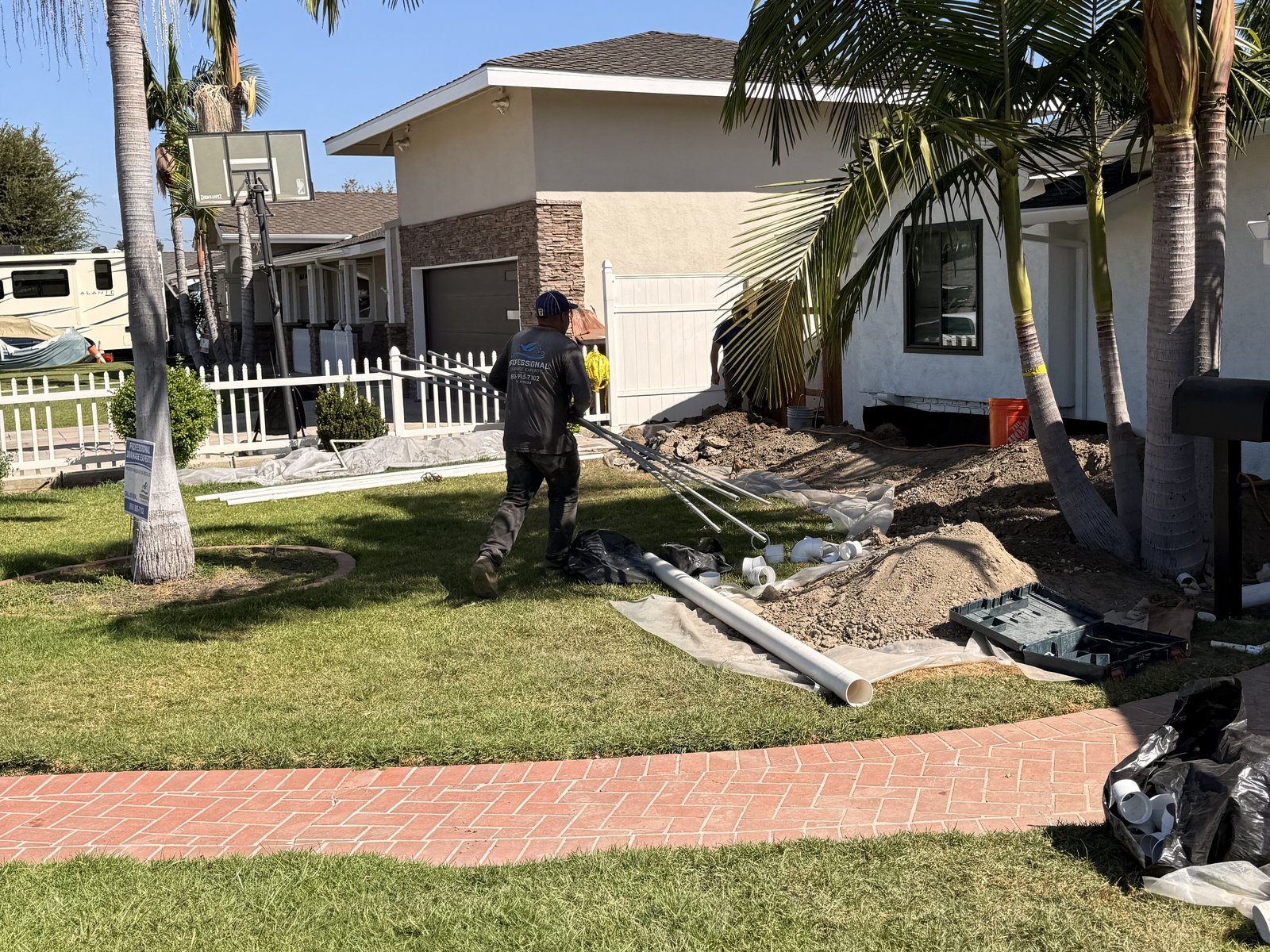 Crew member carrying piping at a front-yard drainage jobsite