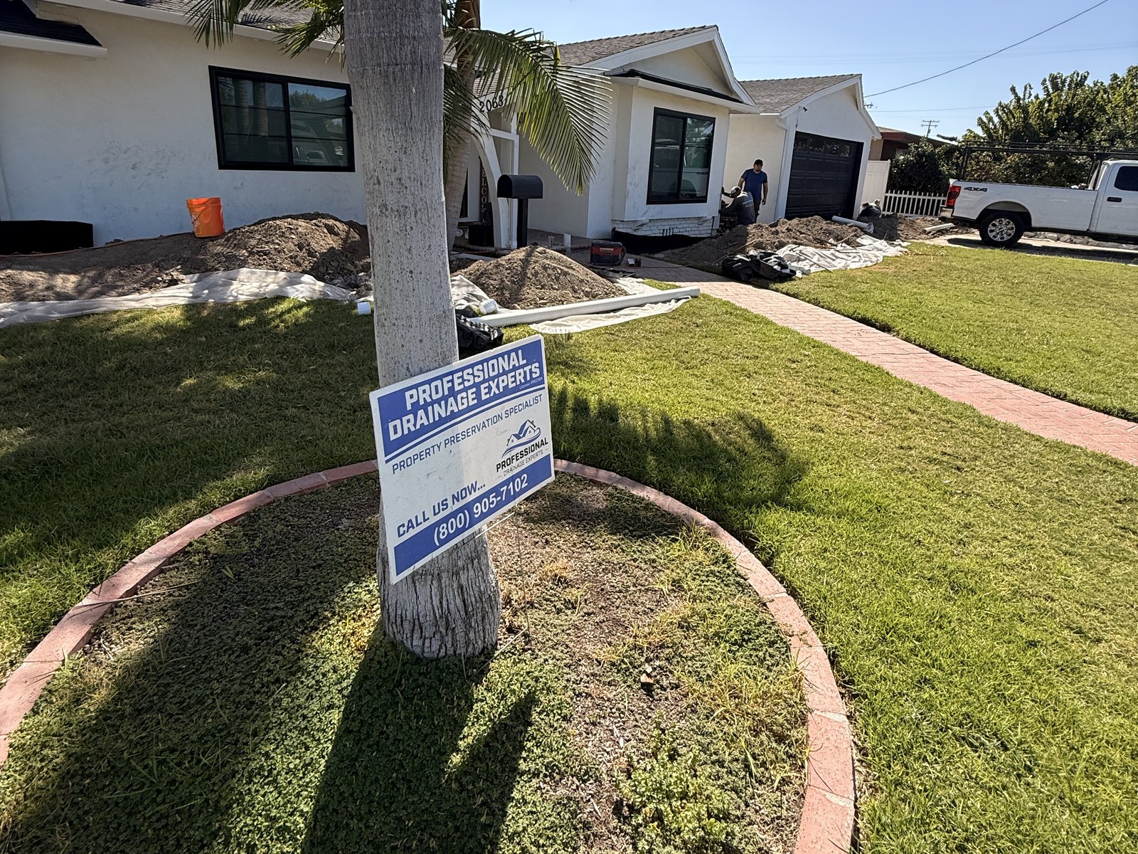 Front-yard excavation underway with a Professional Drainage Experts job sign
