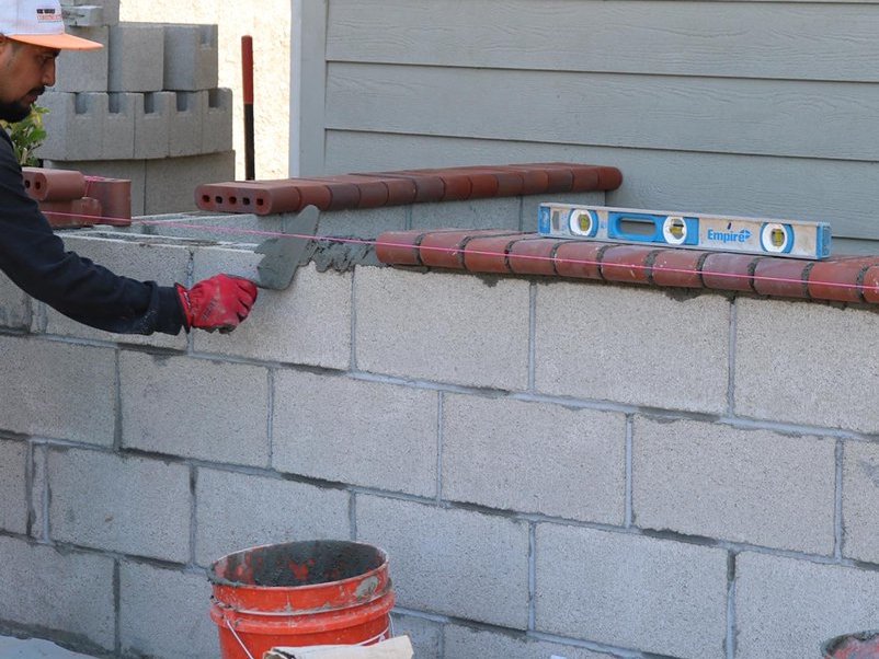 Crew member laying block and checking level on a new masonry wall