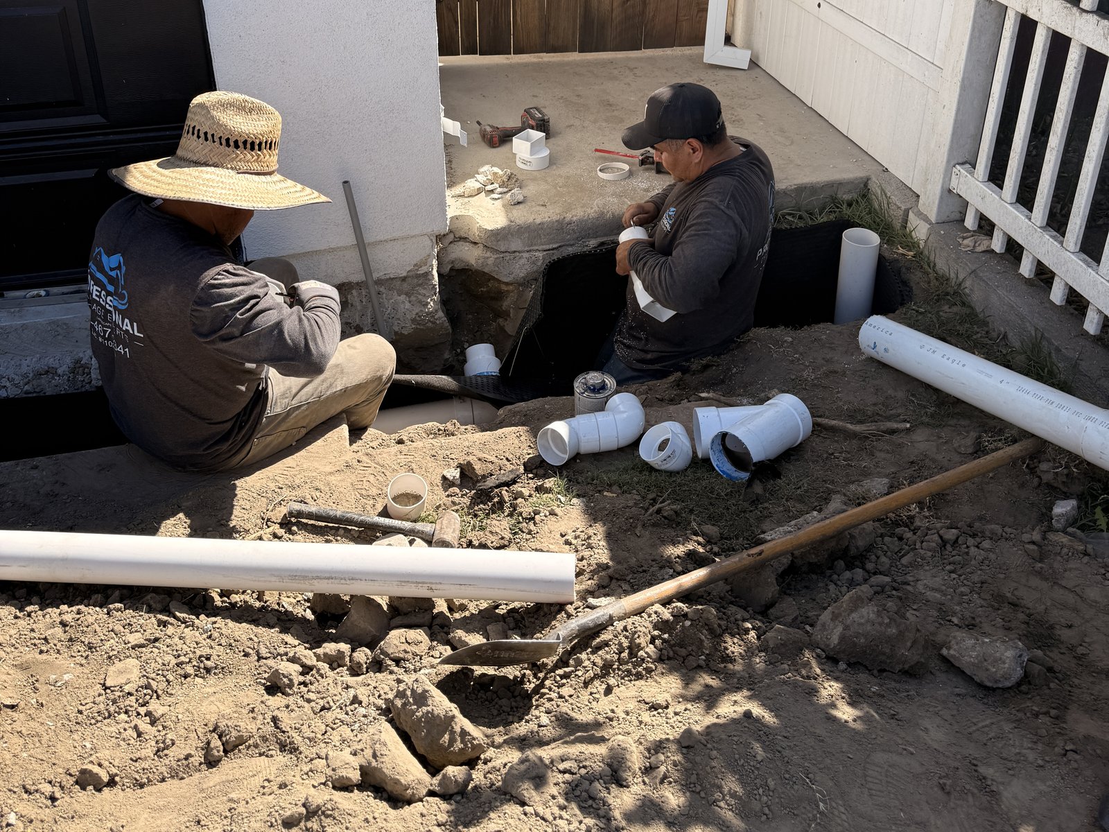 Crew assembling PVC drain line fittings in a side yard